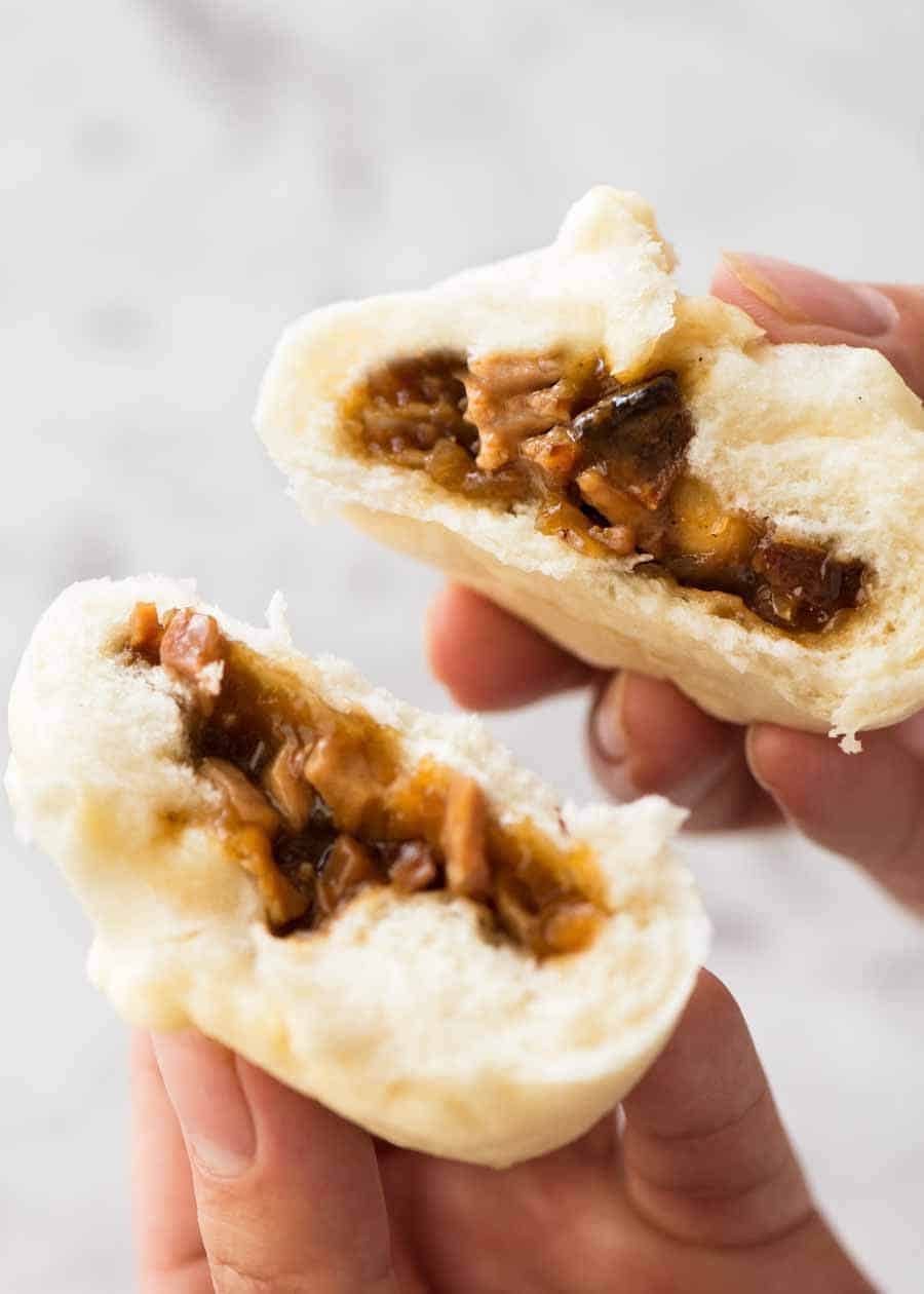 Hand holding a Chinese Steamed Pork Bun broken in half to show the pork filling inside